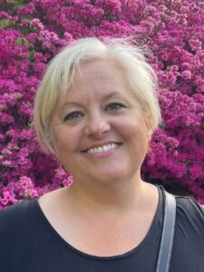 Picture of our head tutor, smiling with blonde hair shown from the shoulders up, wearing black in front of a blooming pink bush. Picture of our head tutor, smiling with blonde hair shown from the shoulders up, wearing black in front of a blooming pink bush.